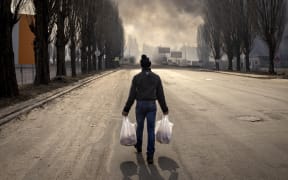A man walks holding bags near a burning warehouse hit by a Russian shell in the suburbs of Kyiv on 24 March,