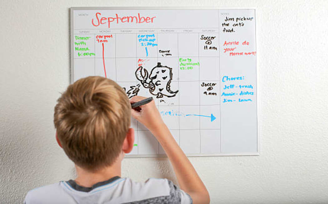 Boy drawing on daily schedule dry erase whiteboard calendar