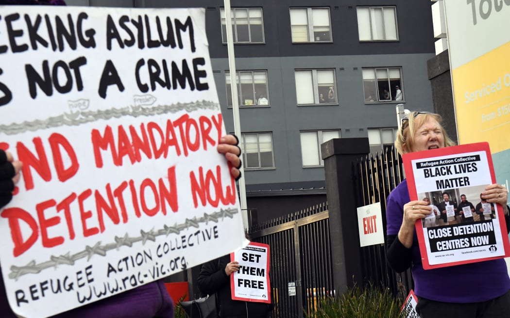 People hold up placards during a pro-refugee rights protest in Melbourne on June 13, 2020 as several asylum seekers who were evacuated for medical reasons from offshore detention centres on Nauru and Manus Island, look down from the hotel where they have been detained.