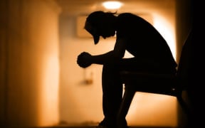 the silhouette of an young man, sitting with his head in his hands, wearing a baseball cap