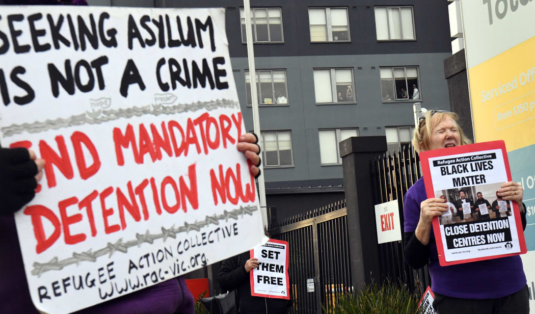 People hold up placards during a pro-refugee rights protest in Melbourne on June 13, 2020 as several asylum seekers who were evacuated for medical reasons from offshore detention centres on Nauru and Manus Island, look down from the hotel where they have been detained.