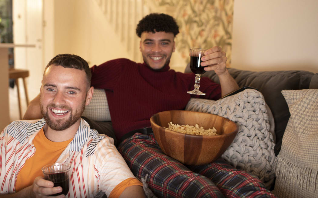 Happy gay male couple with wine and popcorn watching movie. (Photo by Sam Edwards/CAIA IMAGE/SCIENCE P / NEW / Science Photo Library via AFP)