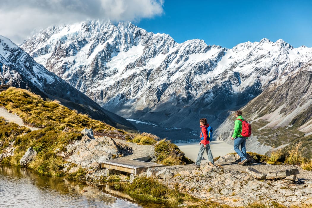 Hiking travel nature hikers in New Zealand mountains. Couple people walking on Sealy Tarns hike trail route with Mount Cook landscape, famous tourist attraction.
