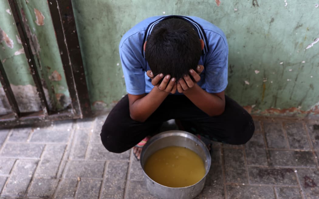 A displaced Palestinian child sits next to a pot of lentil soup that he received at a food distribution point in Gaza City in the northern Gaza Strip.