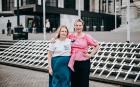 Jane Ludemann and Tash Crosby stand in Parliament grounds in front of 182 white crosses representing the number of people who died of ovarian cancer in 2020.