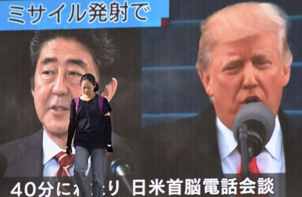 A woman walks in front of a huge screen displaying Japanese Prime Minister Shinzo Abe (L) and US President Donald Trump (R) in Tokyo.