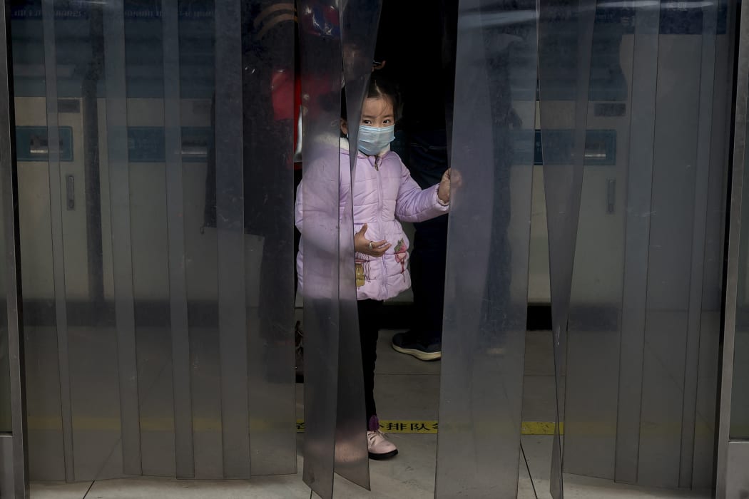 A young girl wearing a protective mask peaks through a plastic curtain at the Beijing railway station on January 27, 2020.