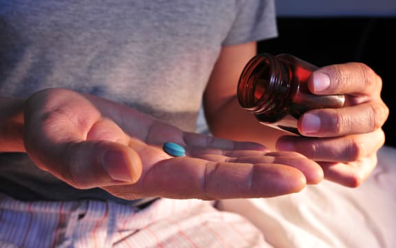 A young man in pajamas in bed about to take a blue pill.