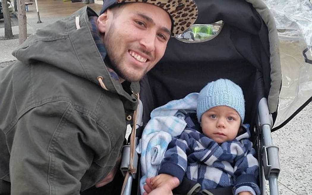 Father crouches smiling by push chair with young son