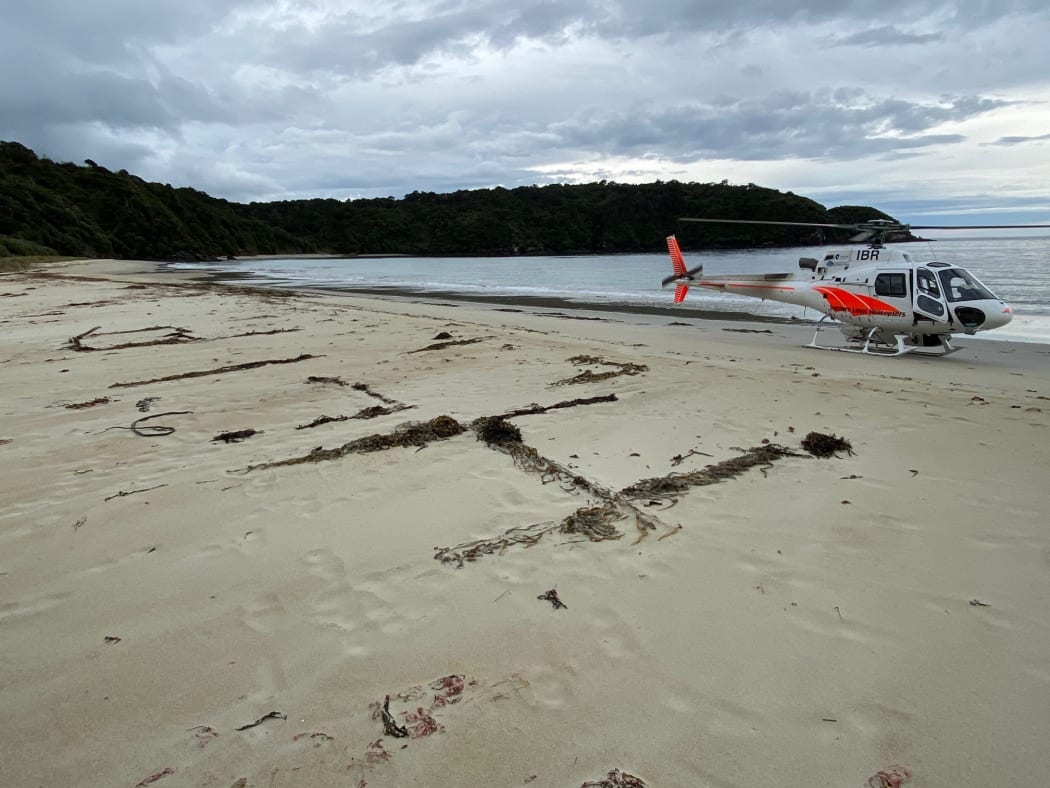 A 'help' sign is written in sand on Chew Tobacco Bay in Stewart Island beside a rescue helicopter.