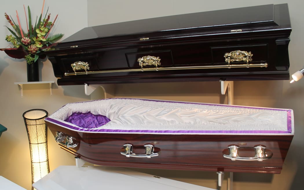Coffins on wall brackets. One dark shint wood the other other open to show plush material inside