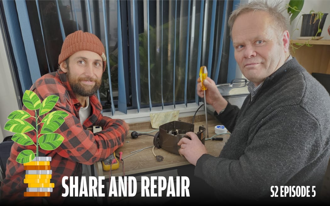 Two men are sitting at a bench, one of them working on a disassembled retro vaccum cleaner with a screwdriver. They are at Repair Riverlution, a Repair Cafe in Richmond, Christchurch where people can bring damaged or broken items to be fixed by volunteers.