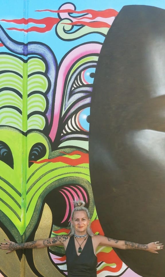 Xoë Hall stands in front of an example of her street art.