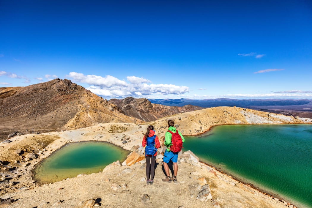 New Zealand popular tourist hiking hike in Tongariro Alpine Crossing National Park. Tramping trampers couple hikers walking on famous destination in NZ.