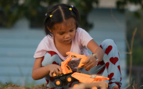 A young girl plays with a large toy truck in a sandpit.