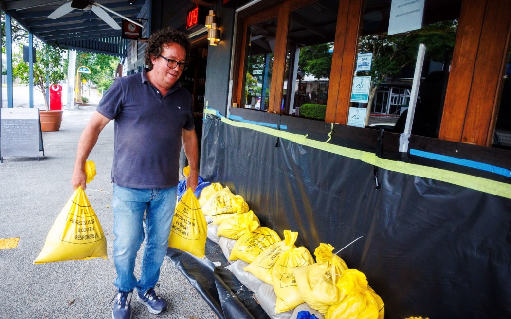Wine merchant Gerard McCord places sandbags in front of his store in Brisbane on March 6, 2025, as tropical cyclone Alfred approaches. The outer fringe of a tropical cyclone started whipping eastern Australia on March 6, bringing drenching rains and record-breaking waves to a heavily populated region rarely hit by typhoons. (Photo by Patrick HAMILTON / AFP)