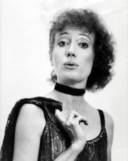 A short haired woman with choker and jacket slung over her shoulder gives a sassy look to the camera.