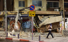 An Israeli rescuer walks in front of a damaged shop in Tel Aviv, after it was hit by a rocket fired by Palestinian militants from the Gaza Strip on October 7, 2023. Palestinian militant group Hamas launched a surprise large-scale attack against Israel on October 7, firing thousands of rockets from Gaza and sending fighters to kill or abduct people as Israel retaliated with devastating air strikes. (Photo by JACK GUEZ / AFP)