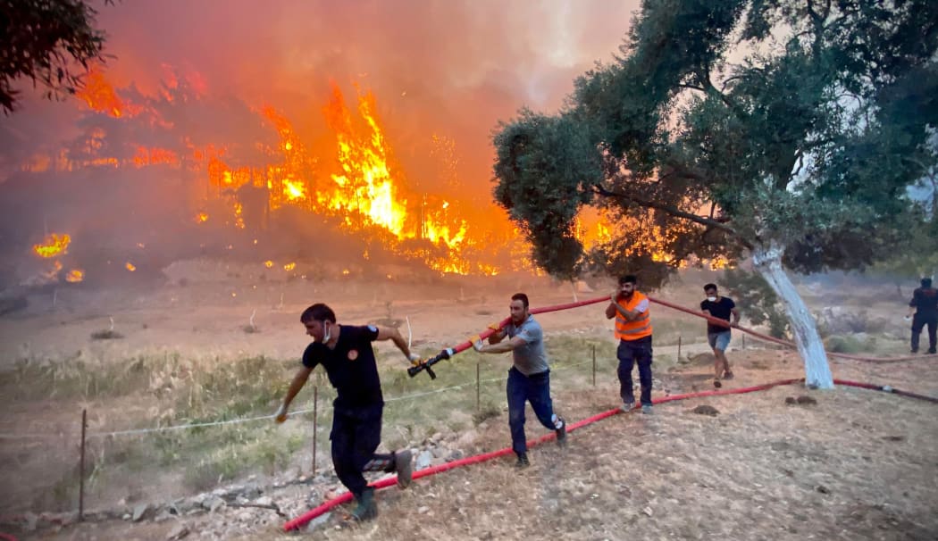 Firemen and local volunteers carry hosepipes as they fight to extinguish a wildfire in Oren, in the holiday region of Mugla, on August 6, 2021 as Turkey struggles against its deadliest wildfires in decades.