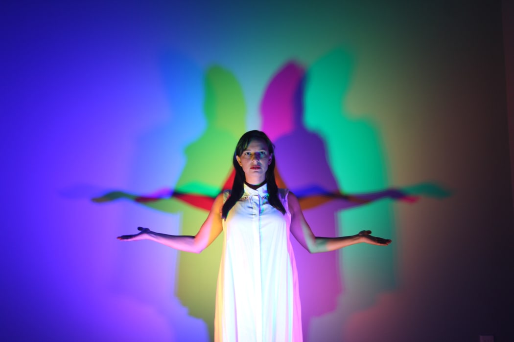 Woman in a white dress holding hands out with lights and CYMK shadows projected on the wall
