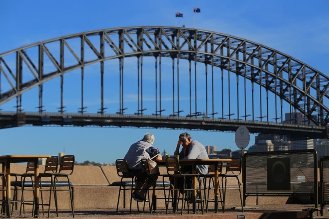 SYDNEY, AUSTRALIA - MARCH 19: An elderly couple sit at a table in front of the Sydney Harbour Bridge, following an outbreak of coronavirus (COVID-19), in Sydney, Australia.