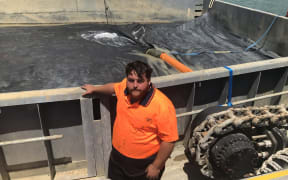 Andrew Johnson with the huge sealed geotech bag on his barge made in Thames slowly starting to fill up with mixed caulerpa, sediment and seawater dredgings from the Omākiwi Cove seafloor. The 1.5m high wall around the bag provides added protection against tiny pieces of caulerpa being spread around as the plants are gently vacuumed up