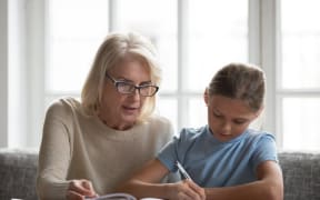 Middle-aged private tutor in glasses helping schoolchild with homework.