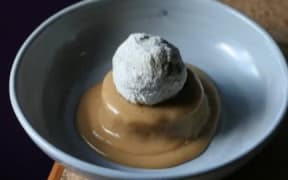 A bowl containing a sugary, deep fried feijoa on a bed of custard.