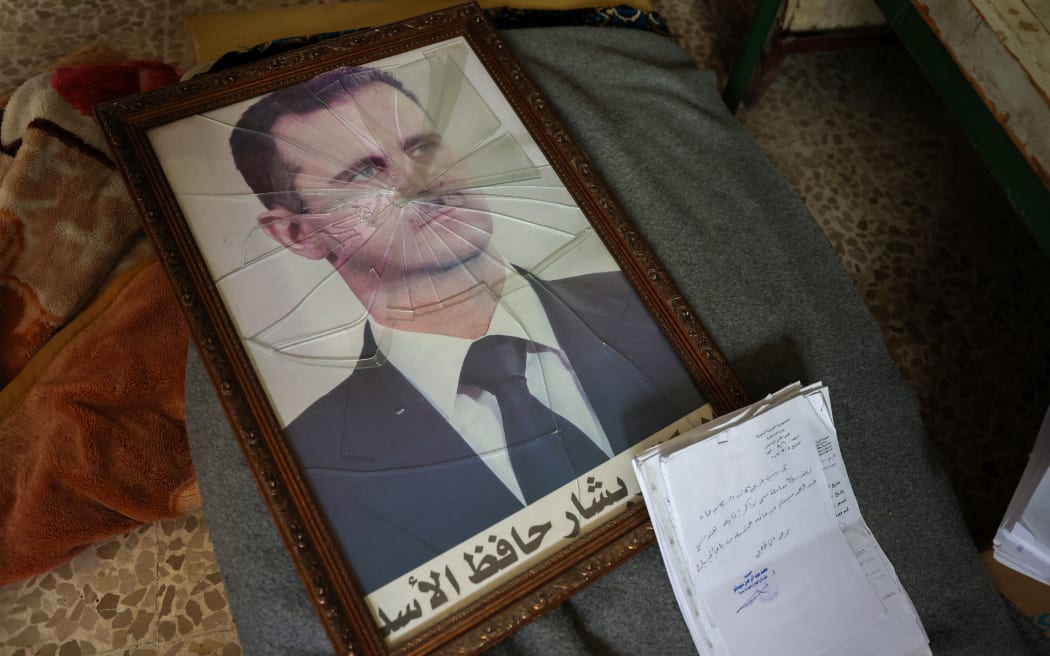 A portrait of Syrian President Bashar al-Assad is pictured with its frame broken, in a Syrian regime's Political Security Branch facility on the outskirts of the central city of Hama, following the capture of the area by anti-government forces, on December 7, 2024. - Syria's embattled government said on December 7 it was setting up a ring of steel around Damascus, state media reported, as rebels on a lightning advance said they were bearing down on the city. The leader of Hayat Tahrir al-Sham (HTS), the Islamist group which has headed the assault, told fighters to prepare to take Damascus, just over a week into a renewed offensive in the long dormant conflict. (Photo by OMAR HAJ KADOUR / AFP)