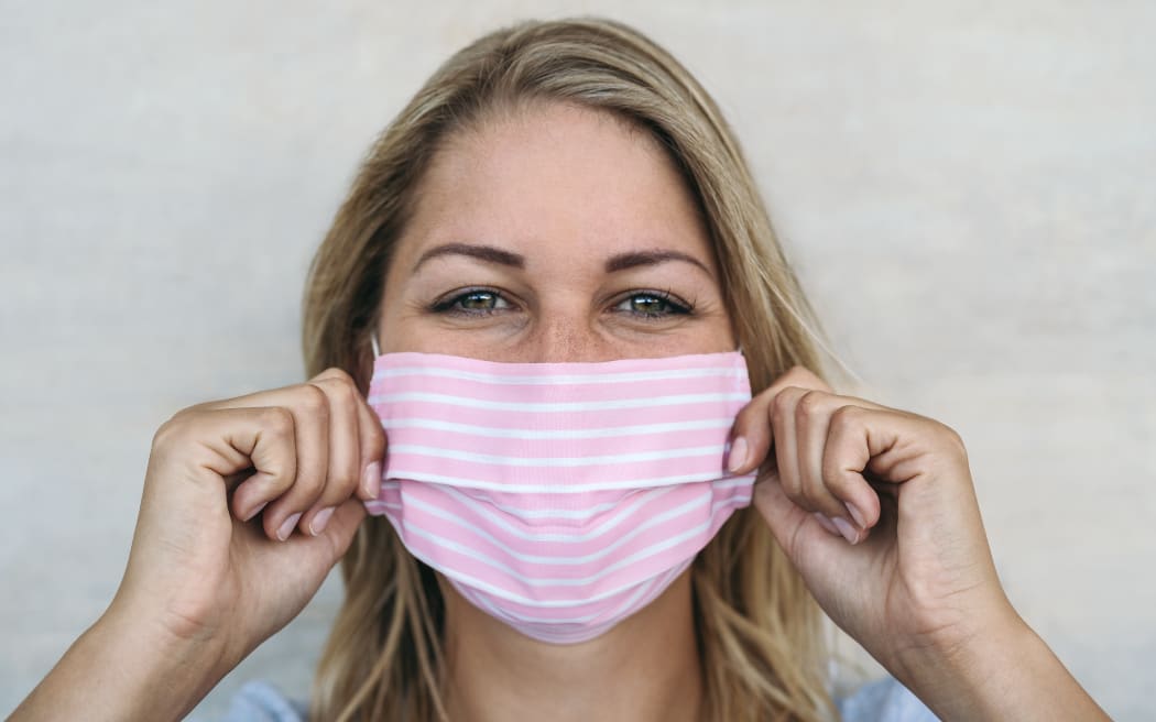 Young woman wearing pink face mask portrait - Blonde female using protective facemask for preventing spread of corona virus