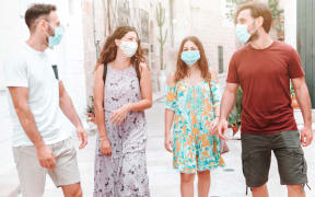 Group of friends stroll through city streets wearing surgical masks - people walk wearing protective equipment during the coronavirus pandemic