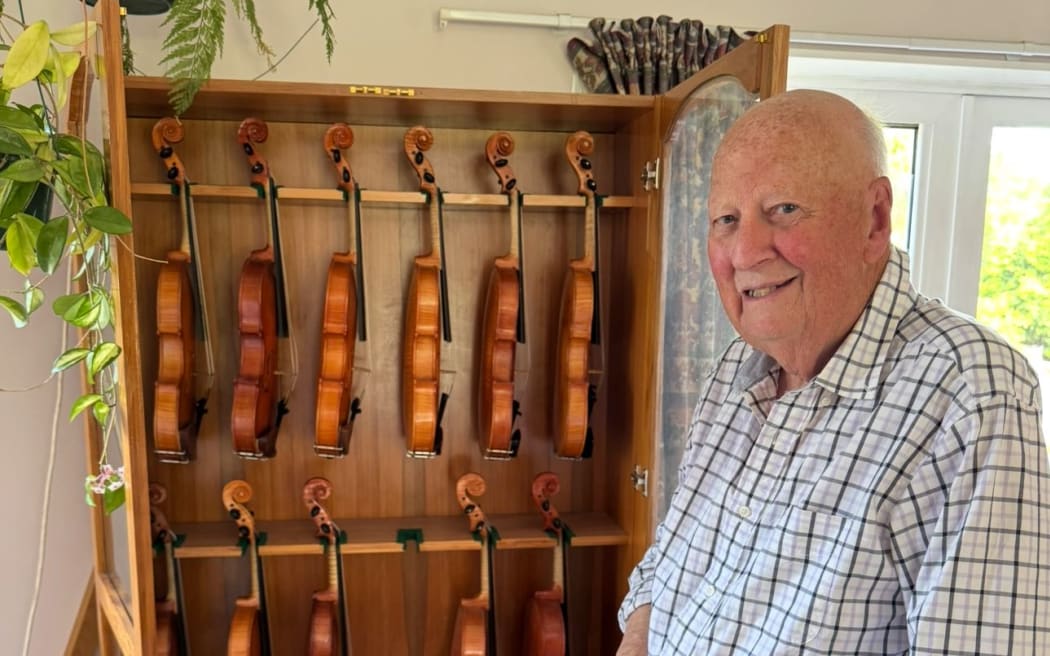Ed Cooke with the cabinet full of violins he personally made.