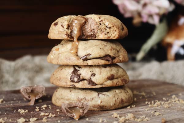 A stack of cookies studded with broken up caramel Easter eggs and tamari almonds on a board.