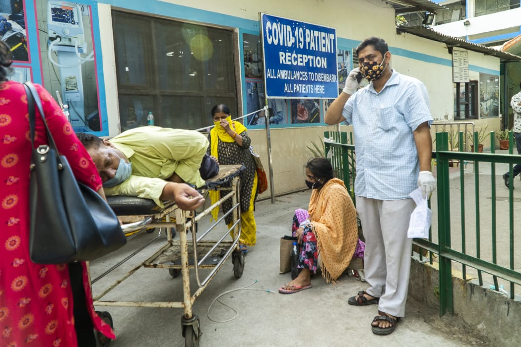In this picture taken on April 23, 2021, relatives wait next to a Covid-19 coronavirus patient laying on a stretcher in a hospital complex for admission in New Delhi.