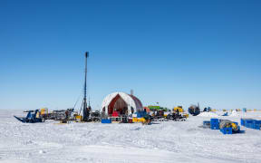 A large half-cylinder tent next to a radio pole and an assortment of equipment.
