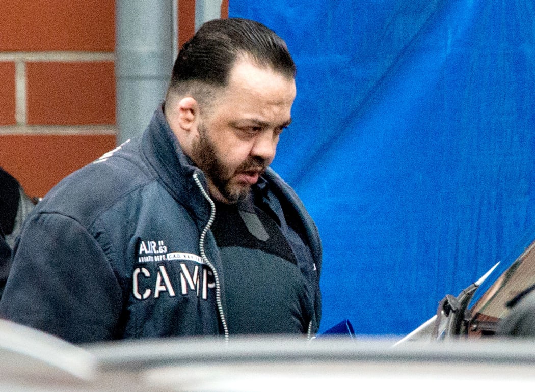 Niels Högel, accused of multiple murders and dressed in a bulletproof vest, is led to the prisoner transporter by judicial officers.