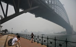 Tourists wearing masks take photos under the Harbour Bridge enveloped in haze caused by nearby bushfires, in Sydney on December 10, 2019.