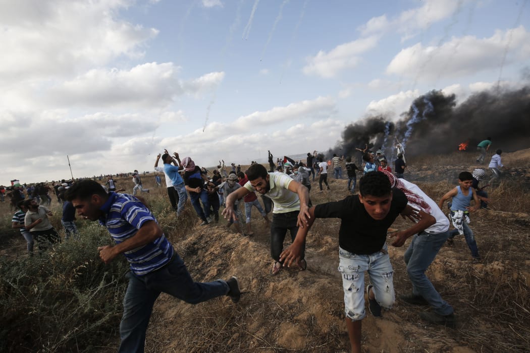 Palestinian protesters flee from incoming tear gas canisters during clashes following a demonstration along the border with Israel east of Khan Yunis in the southern Gaza strip on June 1, 2018. / AFP PHOTO / SAID KHATIB