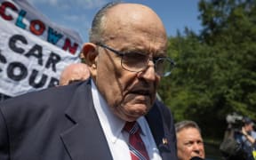 Rudy Giuliani in front of a banner reading 'clown car'.