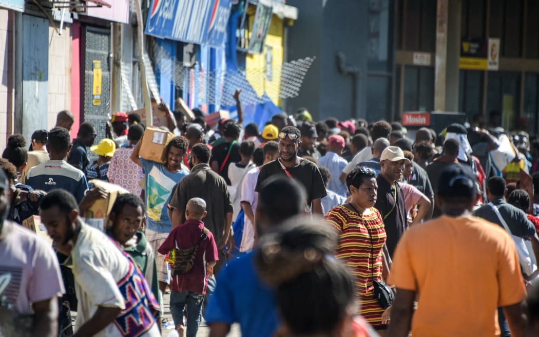 People carry items as crowds leave shops with looted goods amid a state of unrest in Port Moresby on January 10, 2024. A festering pay dispute involving Papua New Guinea's security forces on January 10 sparked angry protests in the capital, where a crowd torched a police car outside the prime minister's office. By Wednesday afternoon pockets of unrest had spread through the capital Port Moresby, with video clips on social media showing crowds looting shops and stretched police scrambling to restore order. (Photo by Andrew KUTAN / AFP)
