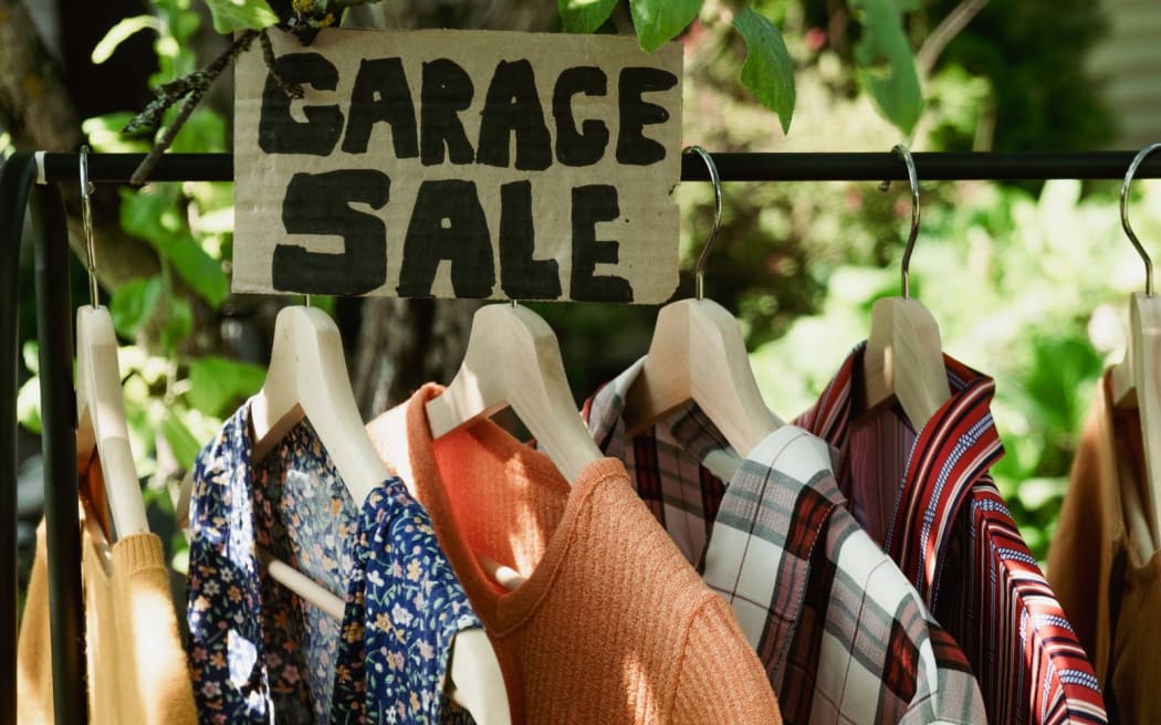 Garage sale, clothes for sale hanging on hanger outdoors.