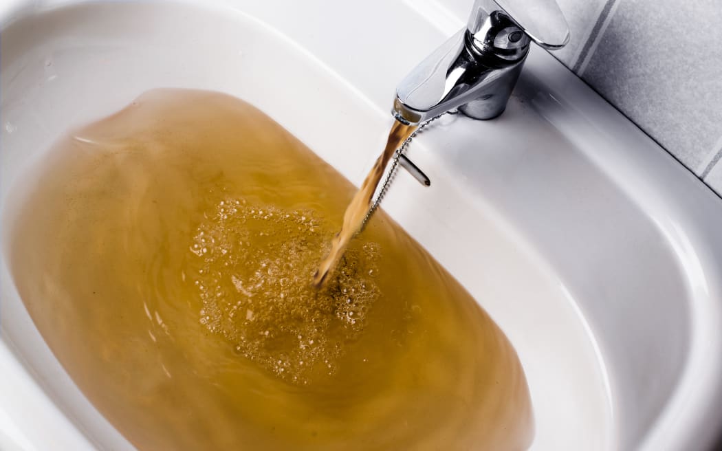 Dirty brown water running into a white sink. Looks very unhealthy,