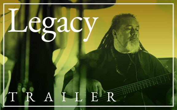 A singer and guitarist stands in front of a large outdoor crowd in the evening. Text reads "Legacy. Trailer".