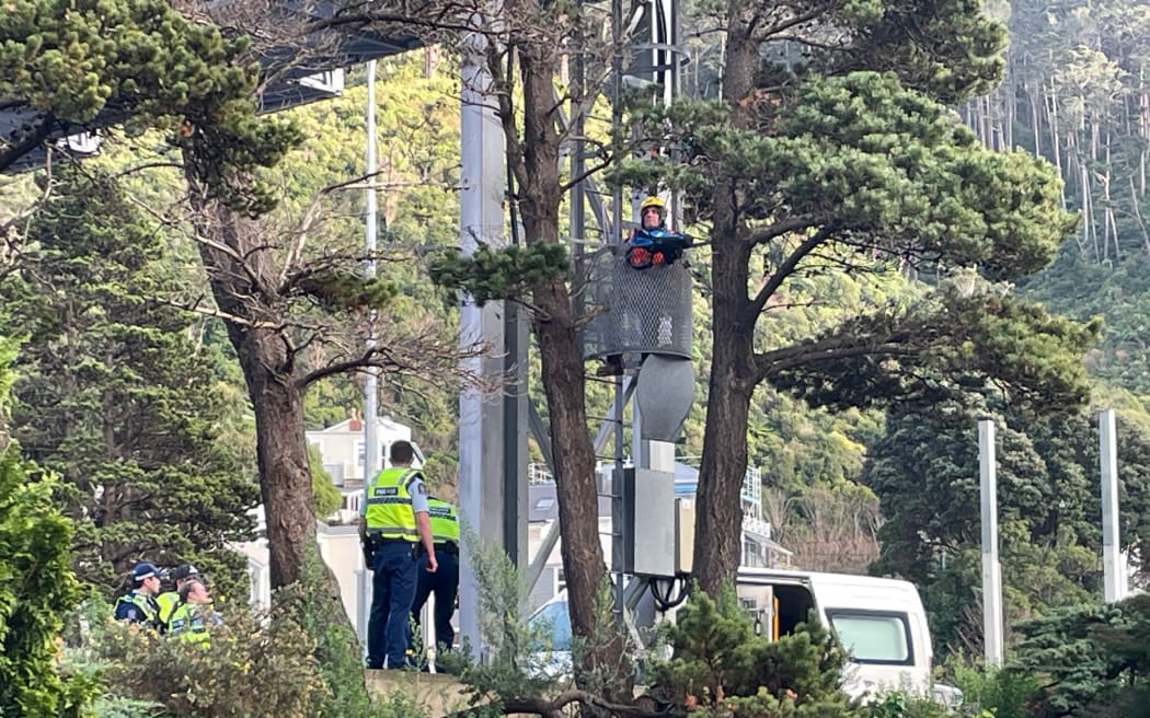 Police speaking with a Restore Passenger Rail protester harnessed to the side of a gantry on Wellington's urban motorway, 31 August 2023.