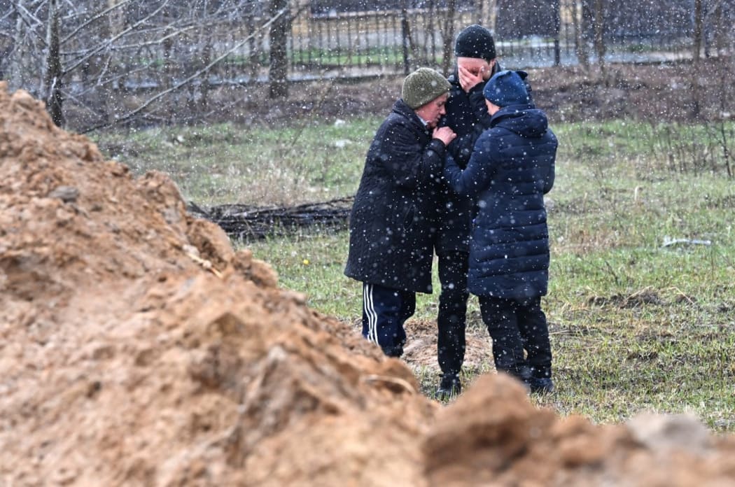 People gather close to a mass grave in the city of Bucha, just northwest of the Ukrainian capital Kyiv on 3 April, 2022.
