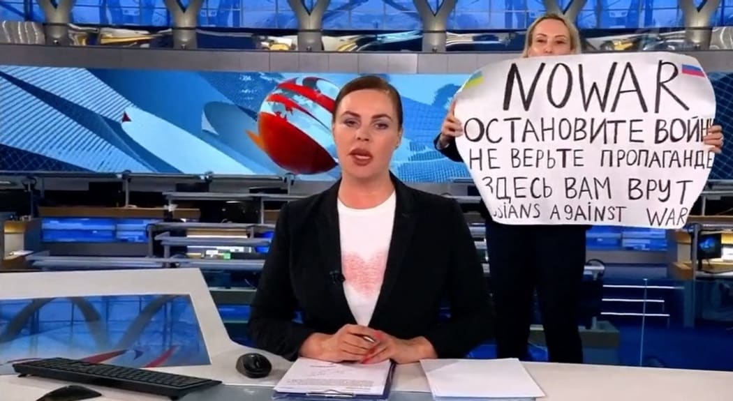 An unidentified woman runs out behind the back of the news anchor woman during on-air news on Monday March 14, 2022 evening news program at the Russia state television Channel One.
