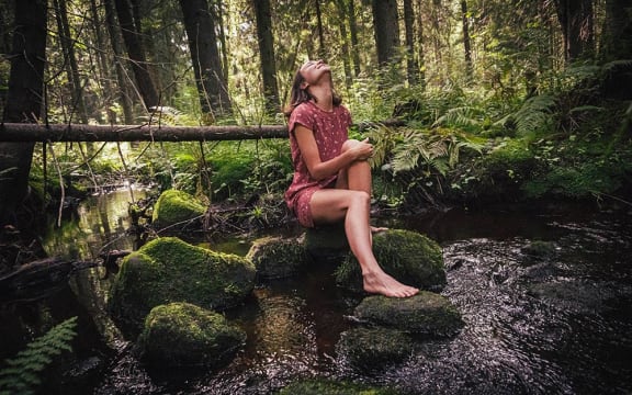 A white female with bare legs sits on moss while looking upwards