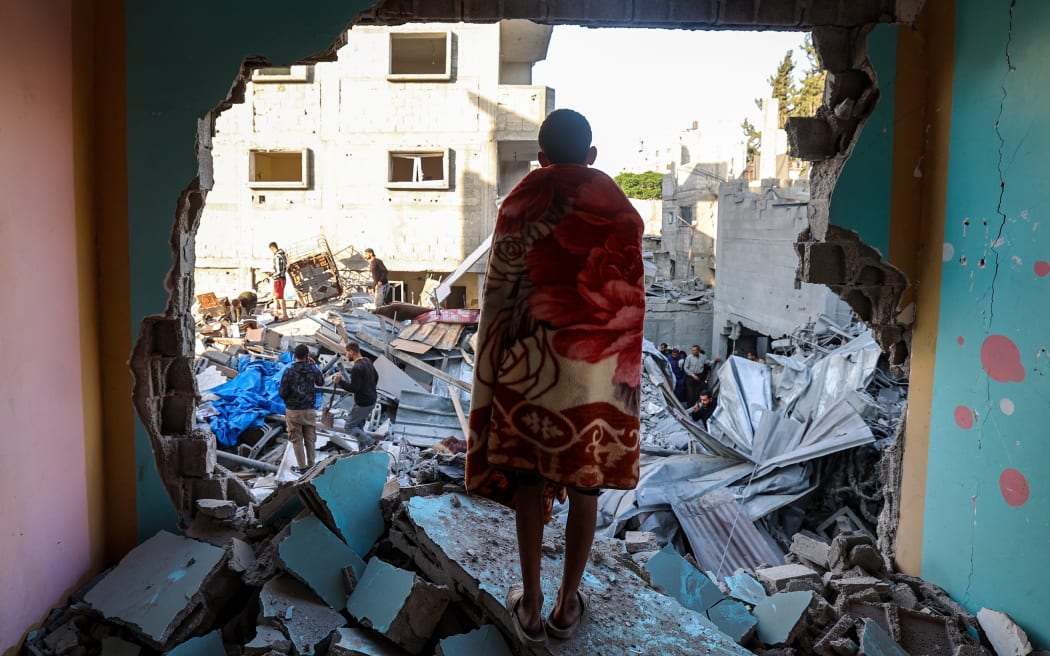 A youth draped in a blanket looks on as people look for survivors in the rubble of a building hit in an Israeli strike in the Bureij camp for Palestinian refugees in the central Gaza Strip on May 2, 2025. (Photo by Eyad BABA / AFP)