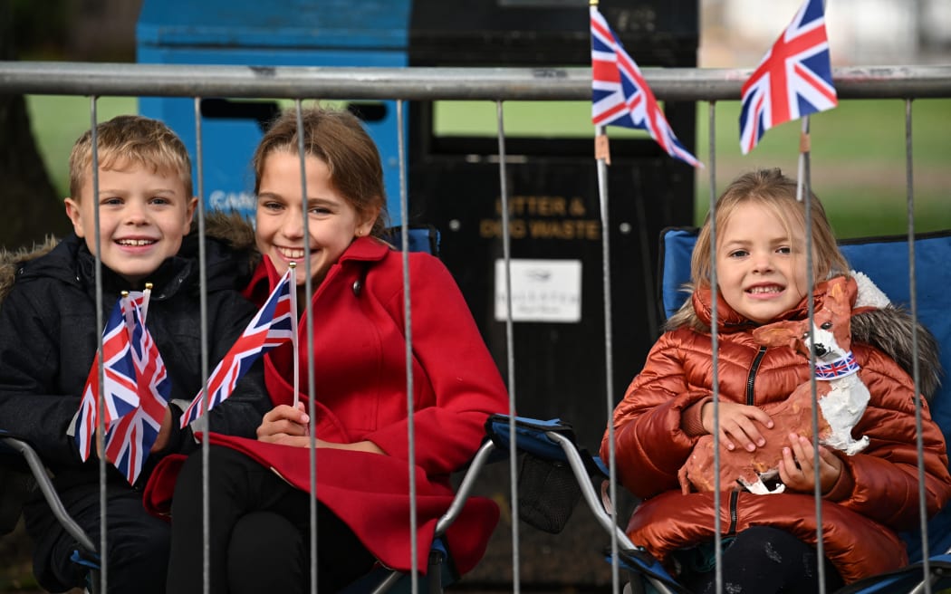 Children sit behind barriers in Ballater on September 11, 2022 as they wait for Queen Elizabeth II's coffin to travel through the Scottish village. - Queen Elizabeth II's coffin will travel by road through Scottish towns and villages as it begins its final journey from her beloved Scottish retreat of Balmoral. Mourners are expected to line the streets to watch a hearse carrying her oak coffin wend its way through Aberdeenshire, Aberdeen and Dundee on the way to Edinburgh. (Photo by Paul ELLIS / AFP)