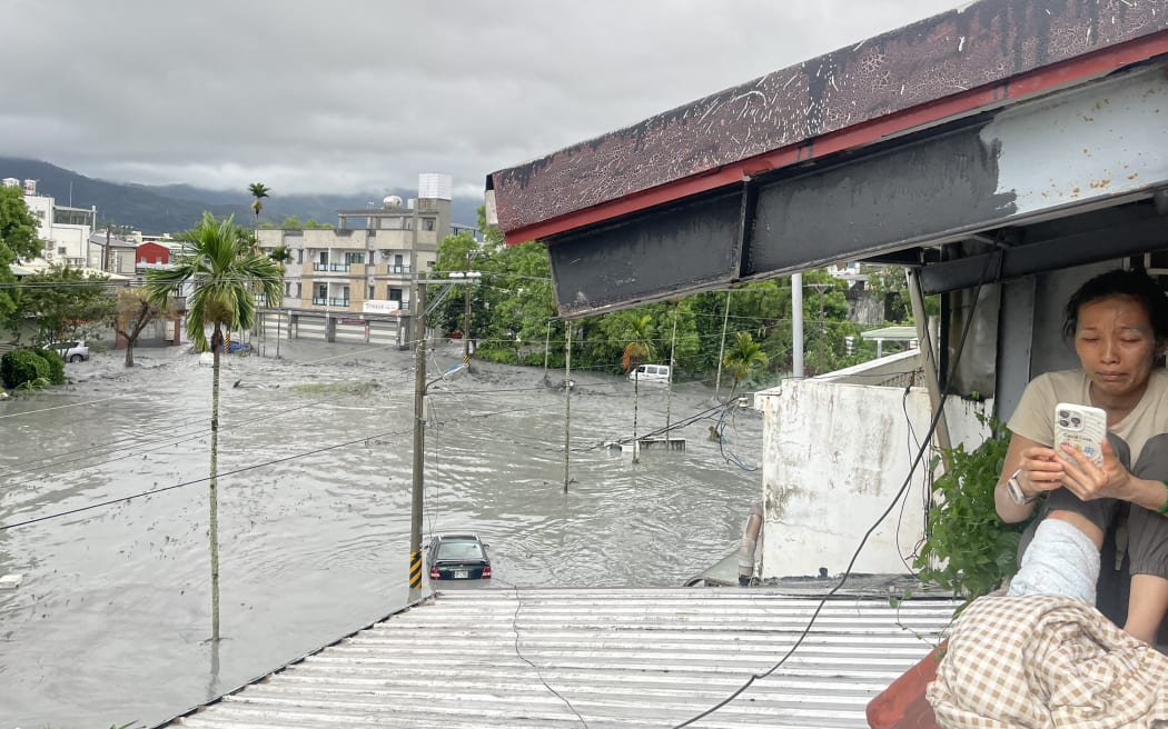 A resident uses her mobile phone while sitting on the roof of a house, as water from a burst landslide dam overflows and floods the area in Hualien on September 23, 2025, as a result of heavy rain due to Super Typhoon Ragasa. The super typhoon was generating maximum sustained winds of 220 kilometres (137 miles) per hour near its centre while moving west across the South China Sea, according to Hong Kong's weather service.